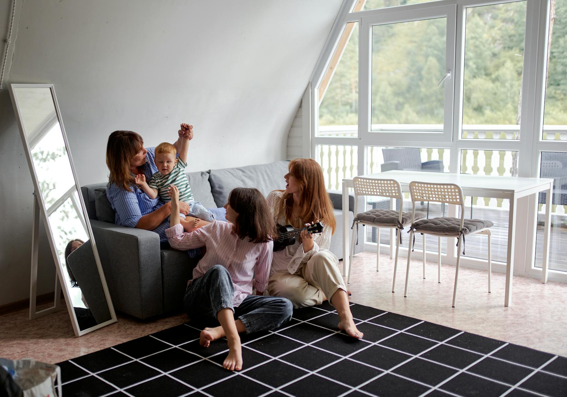 Grandma with toddler child near female relatives on rug spending time together in countryside house